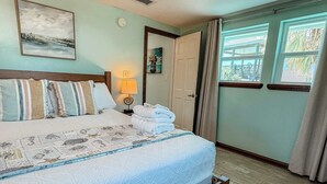 A neatly made bed with a patterned quilt, a bedside lamp, and a view of the outdoors through a window. - St.George Island Bayfront Paradise with Pool,Dock (St. Geroge Island)