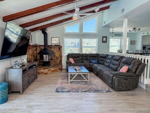A spacious living room with a stone fireplace, a large flat-screen TV, a leather sofa, and a dining area with a white railing.