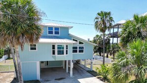 A light blue house with a covered porch and a garage, surrounded by palm trees and a white fence. - St.George Island Bayfront Paradise with Pool,Dock (St. Geroge Island)