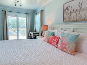 A hotel room with a large bed, a desk, and a view of the outdoors. - St.George Island Bayfront Paradise with Pool,Dock Golf Cart Included (St. Geroge Island)