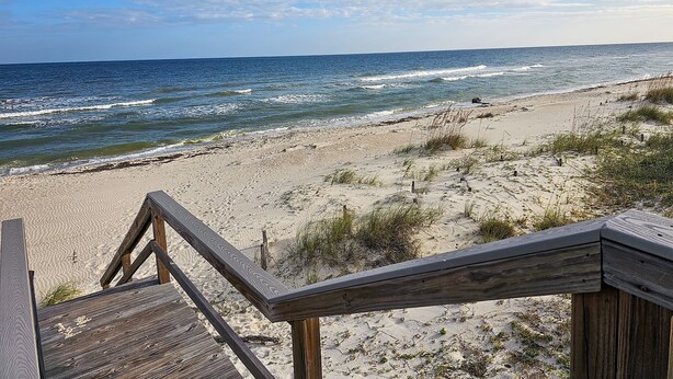 A wooden staircase leading down to a sandy beach with the ocean in the background. - Private Screened Pool, Easy Beach Access in Plantation! (St. George Island)