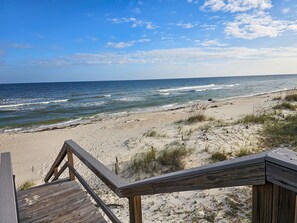 A wooden staircase leading down to a sandy beach with the ocean in the background.