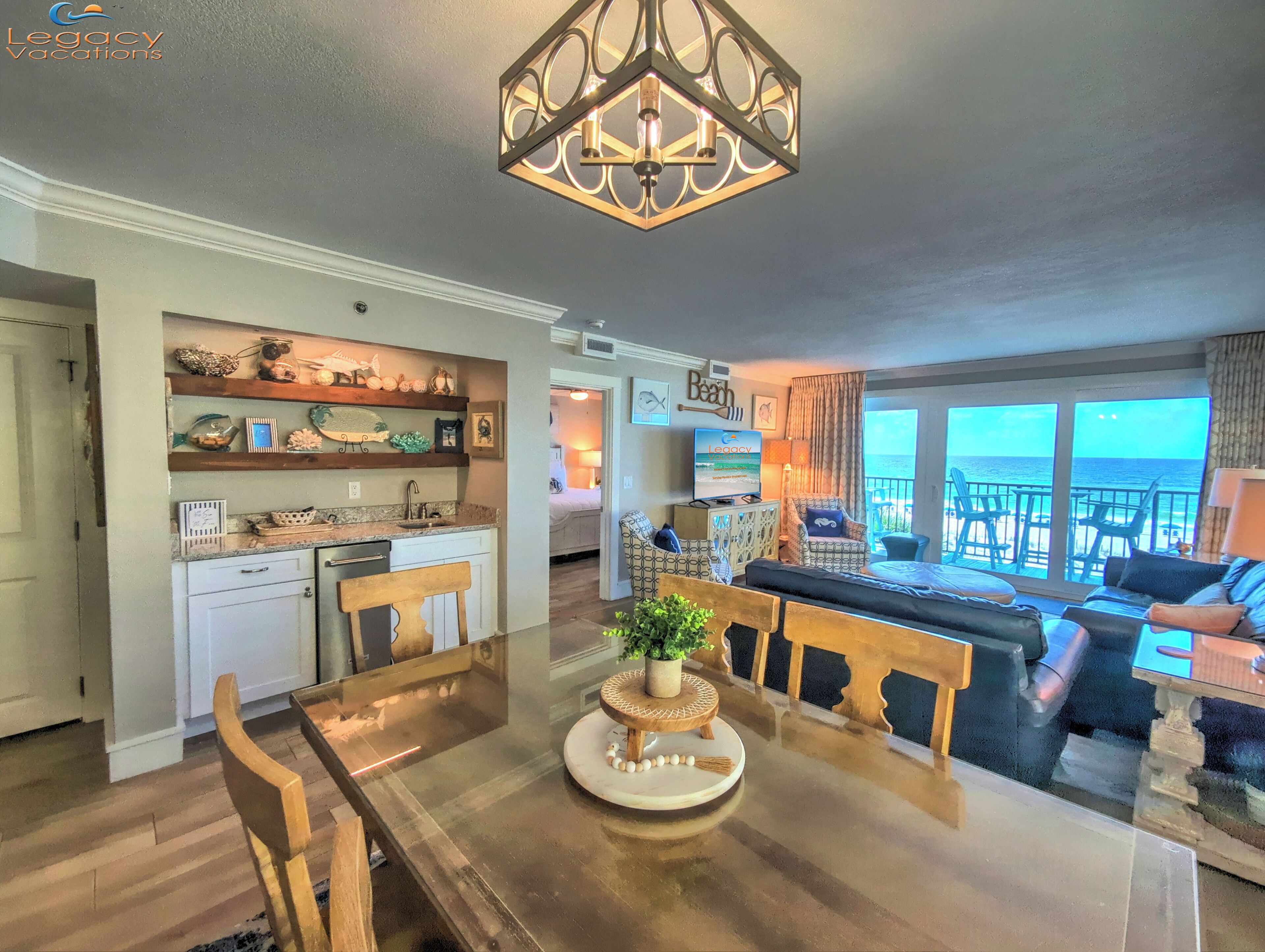 Amplia sala de estar con un ventanal con vista al océano, una mesa de comedor con sillas y una cocina con estantes decorativos.