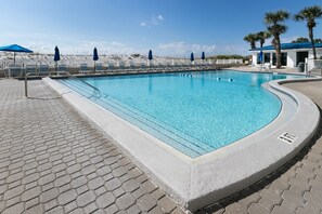 Una piscina con sillas de descanso y sombrillas, rodeada por una valla blanca y palmeras.