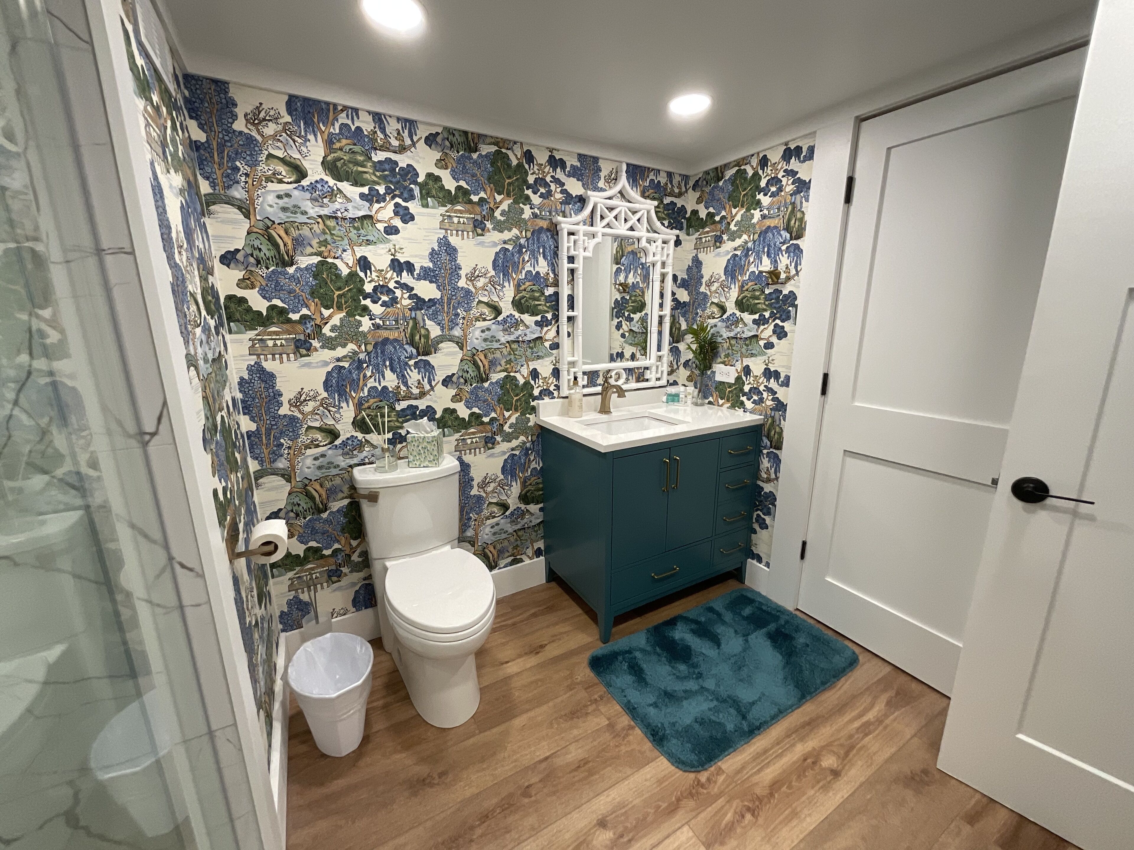 A bathroom with a toilet, sink, and cabinet, featuring a floral wallpaper and wooden flooring.