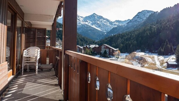 Un balcone in legno con vista su montagne innevate e un piccolo edificio in lontananza.