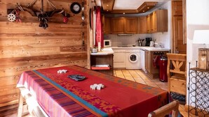 Una camera accogliente con una parete in legno, un tavolo da pranzo con tovaglia rossa e un angolo cottura con pensili in legno e un estintore rosso.