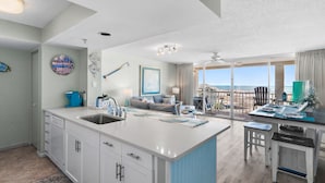 A modern kitchen with a large island, a dining area with a view, and a living room with a sofa and artwork.