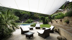 Un área junto a la piscina con muebles de mimbre y una pared de piedra.