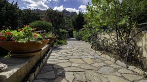 Un sendero de piedra que atraviesa un jardín con macetas de terracota grandes, llenas de flores y abundante vegetación.