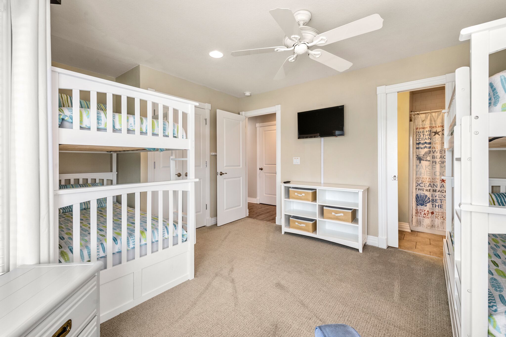A child's bedroom with bunk beds, a ceiling fan, a TV, and storage drawers.
