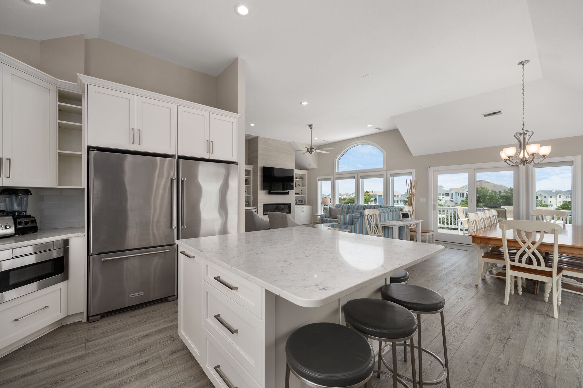 A modern kitchen with white cabinetry, a large island with stools, and a dining area with a view.
