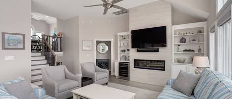 A modern living room with a fireplace, a flat-screen TV, and a ceiling fan.