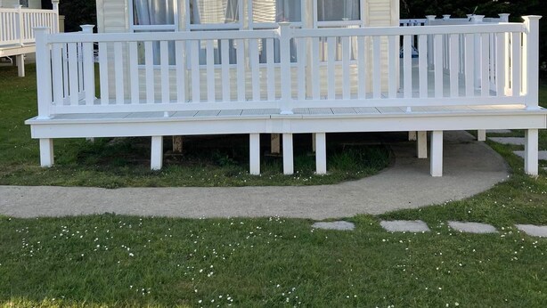A small, single-story mobile home with a white exterior and a covered porch. - 3 Bedroom Ensuite Caravan (Shanklin)