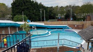 A swimming pool area with multiple pools, a wooden fence, and a sign indicating a 1:2 child ratio. - 3 Bedroom Ensuite Caravan (Shanklin)