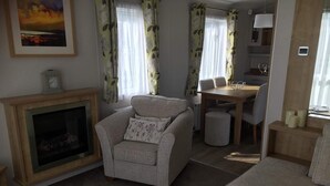 A cozy living room with a fireplace, a dining area with a table and chairs, and a sofa. - 3 Bedroom Ensuite Caravan (Shanklin)