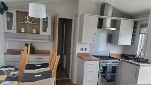 A compact kitchen with a gas stove, oven, and white cabinets. There is a dining area with a table and chairs. - 3 Bedroom Ensuite Caravan (Shanklin)