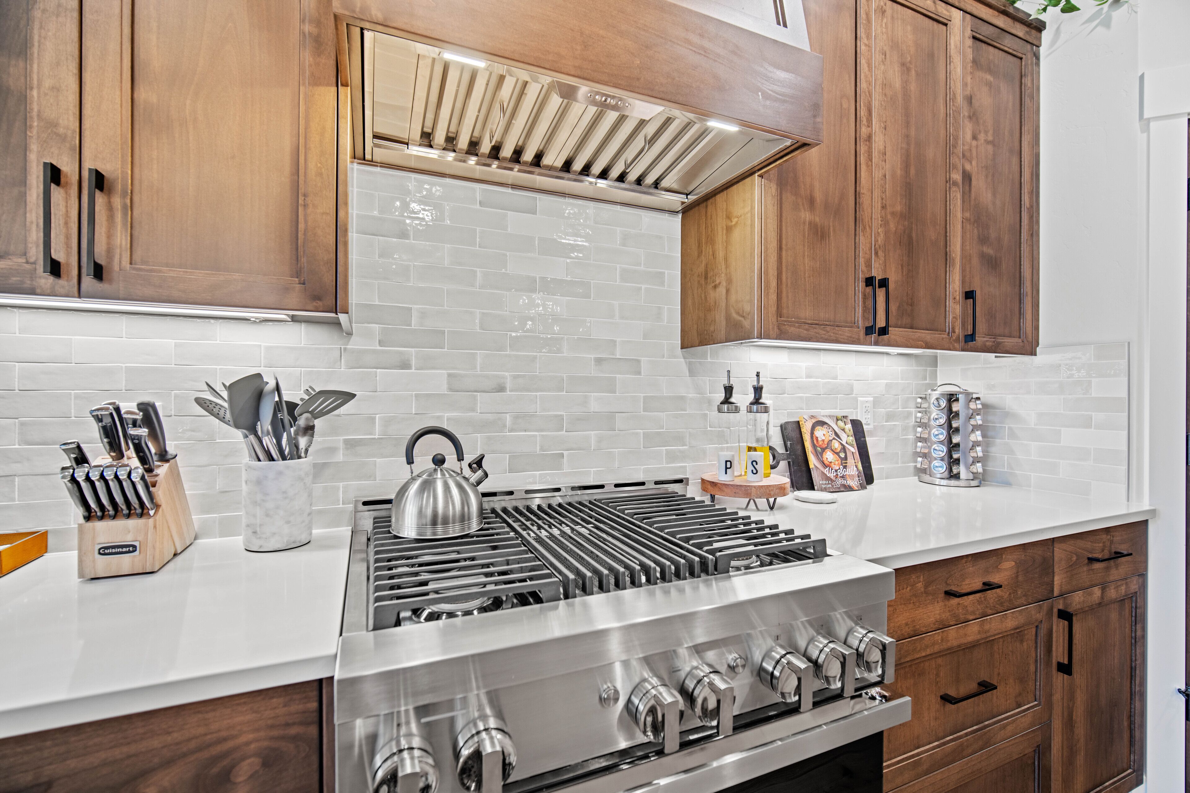 Una cocina moderna con armarios de madera, estufa de acero inoxidable y salpicadero de azulejos blancos.