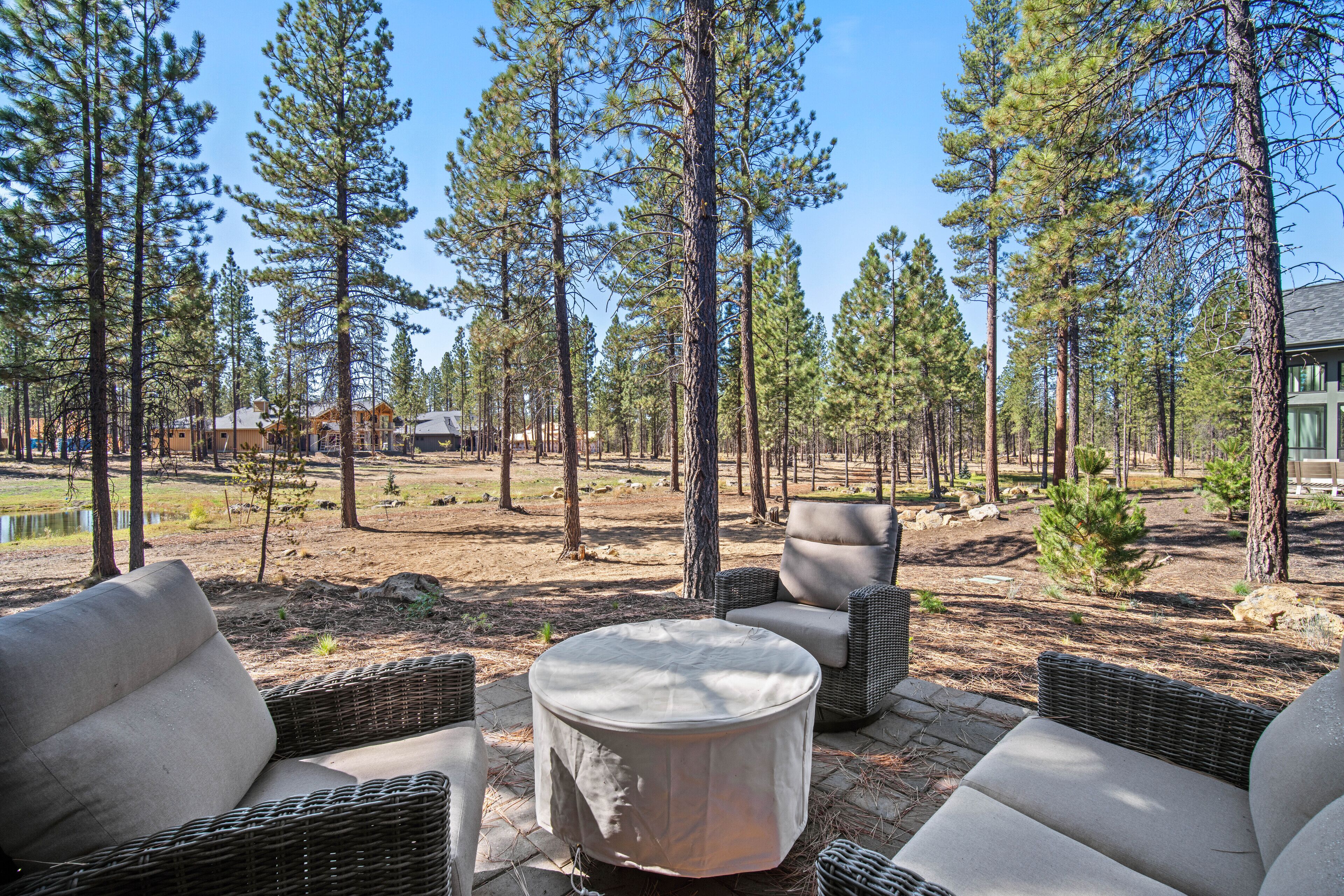 An outdoor seating area with wicker furniture and a round table, surrounded by tall pine trees.