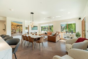 A spacious living area with a dining table, sofas, and a kitchen in the background.