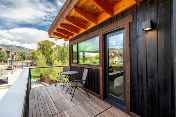 A wooden deck with outdoor seating, a large window, and a view of a mountain landscape.