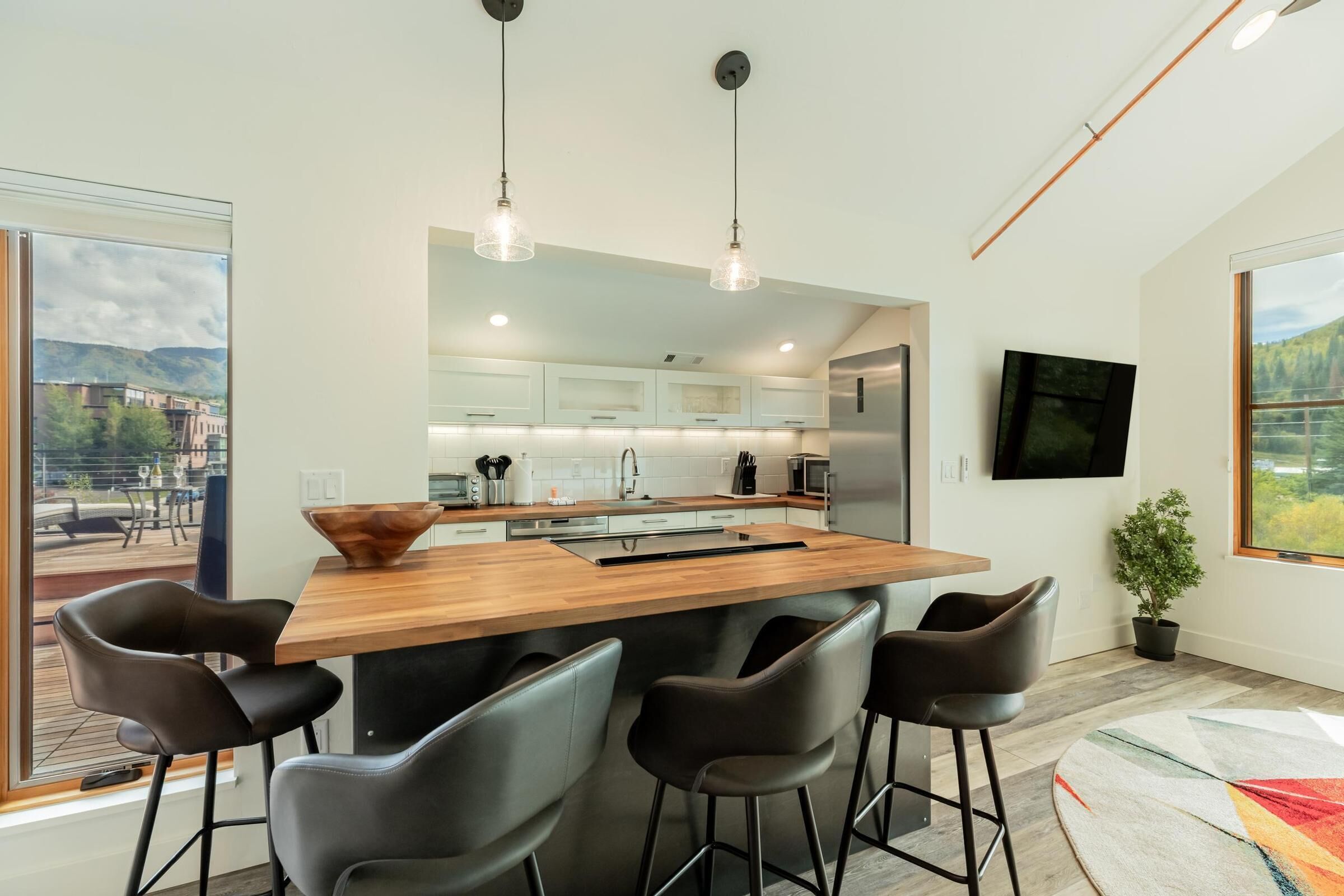 A modern kitchen with a central island, bar stools, pendant lighting, and a view of the city.