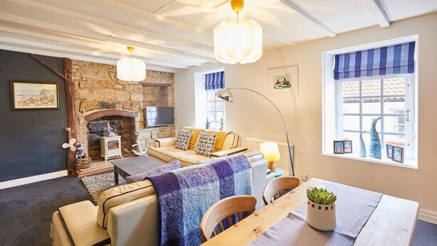 Un salón acogedor con chimenea de piedra, un sofá, una mesa de comedor con sillas y un ventanal con cortinas azules.