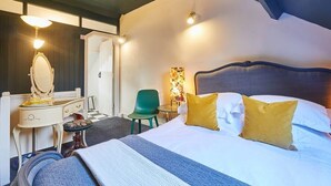Habitación de hotel con cama, escritorio con espejo, silla y mesita de noche con lámpara.