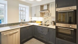 Una cocina moderna con armarios oscuros, lavavajillas de acero inoxidable, horno doble e iluminación colgante.