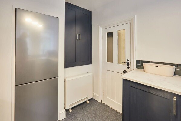 A compact kitchen with a refrigerator, a built-in oven, a white sink, and a dark cabinet.