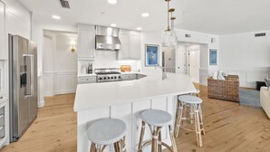 A modern kitchen with a large island, stainless steel appliances, and wicker bar stools. - Gulf and Dune Views Steps from the Beach (Watersound)