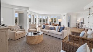 A spacious living room with a large sofa, armchairs, a coffee table, and a dining area with wicker furniture. - Gulf and Dune Views Steps from the Beach (Watersound)