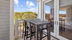 A covered patio with a table and chairs, a glass door leading to an outdoor area, and a view of the surrounding landscape. - Gulf and Dune Views Steps from the Beach (Watersound)
