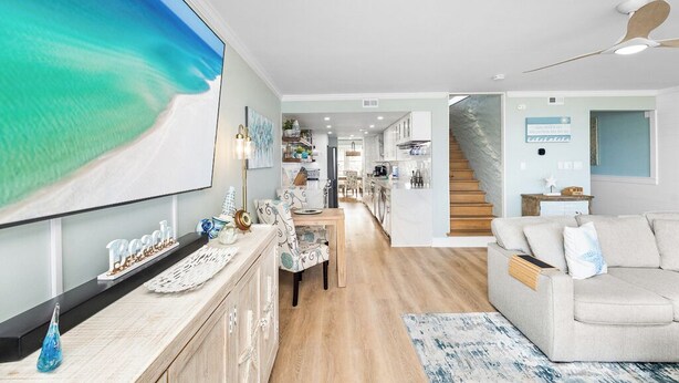 A spacious living room with a large TV, a dining area, and a staircase leading to another level. - Bayfront Escape | Santa Rosa Sound Views | 100 Steps to the Beach! (Pensacola Beach)