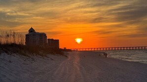 A beach with a sunset, a pier, and a building on the left. - Bayfront Escape | Santa Rosa Sound Views | 100 Steps to the Beach! (Pensacola Beach)