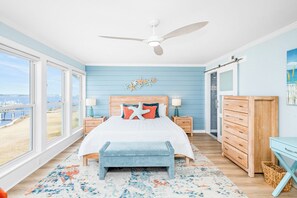 Quarto com uma cama grande, ventoinha no teto, vista para o exterior e cômoda de madeira.