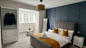 A bedroom with a bed, bedside tables, a wardrobe, a window with blinds, and a hanging light fixture.