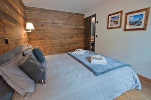 A bedroom with a wooden headboard, a bed with a white comforter, two pillows, a blue throw blanket, and two framed pictures on the wall. - Z Suite - Haus Roger (Zermatt)