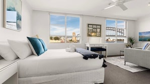 Une chambre d’hôtel moderne équipée d’un lit, d’un bureau, d’un canapé et de grandes fenêtres donnant sur la ville.