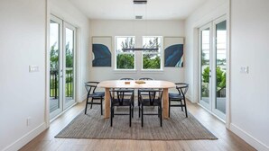 A dining area with a round table, six chairs, and two windows with blinds. - The Ebberly Estate at Lunara Bay (Key West)