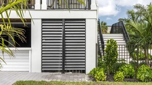 A modern building with a large garage door, a balcony, and a well-maintained garden with various plants. - The Ebberly Estate at Lunara Bay (Key West)