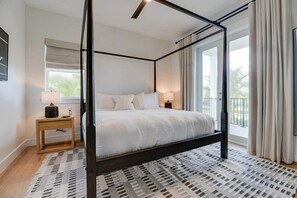 A four-poster bed with a white bedspread, a wooden nightstand with a lamp, and a patterned rug.