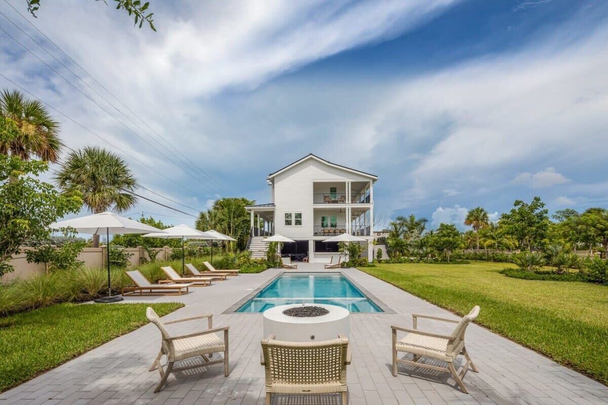 A two-story house with a swimming pool, outdoor seating, and a well-maintained lawn.
