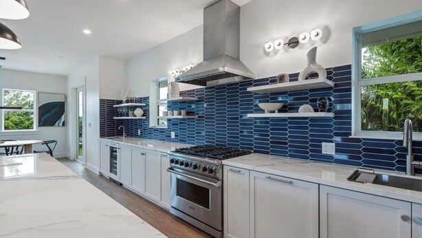A modern kitchen with a stainless steel stove, white cabinets, and blue-tiled backsplash. - The Ebberly Estate at Lunara Bay (Key West)