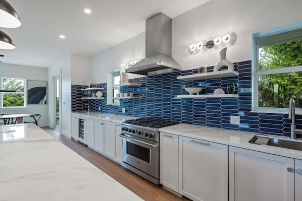 A modern kitchen with a stainless steel stove, white cabinets, and blue-tiled backsplash.