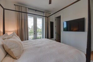 A bedroom with a large bed, a TV mounted on the wall, and a balcony with curtains.