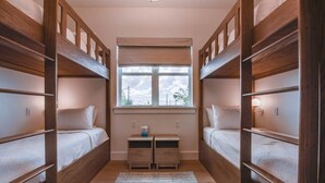 A narrow room with two bunk beds on either side, a small window with a view, and a pair of nightstands with drawers. - The Ebberly Estate at Lunara Bay (Key West)