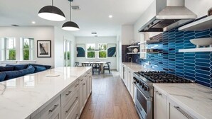 Een moderne keuken met een centraal eiland, een gasfornuis en een blauwe tegelwand.