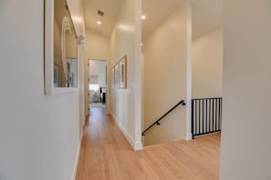 A hallway with wooden flooring, white walls, and a black railing on the right.