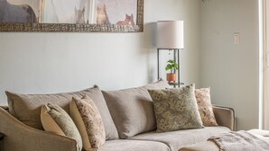 Sala de estar com sofá, almofadas, luminária e um quadro na parede.
